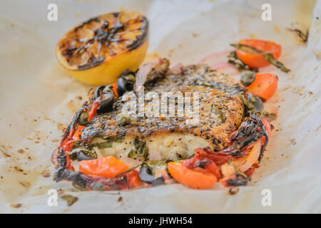 Al Cartoccio frischer Seebarsch Wolfsbarschfilet gekocht in Pergamentpapier mit sonnengetrockneten Tomaten, Sardellen und Kapern Stockfoto