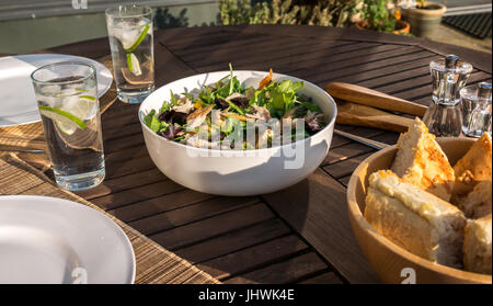 Geräucherte Makrele und Clementine Salat, serviert im Freien in weißes Geschirr Schale auf Deck Tisch mit Tellern, Gläsern, und Baguette Schüssel Stockfoto