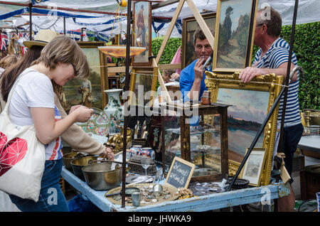 Ein paar Damen durchsuchen Elemente auf eine Antiquitäten-Stall in Portobello Road als Stall Besitzer schauen auf. Stockfoto