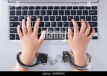 Kind die Hände in Handschellen mit Laptop im Büro Stockfoto