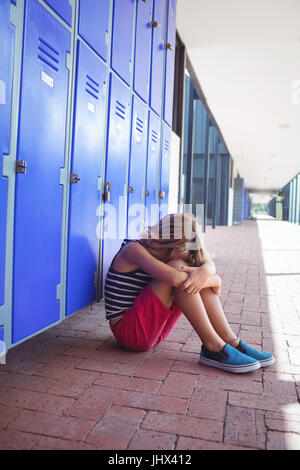 Gesamte Länge der Mädchen sitzen auf Bürgersteig von Schließfächern im Korridor in der Schule Stockfoto