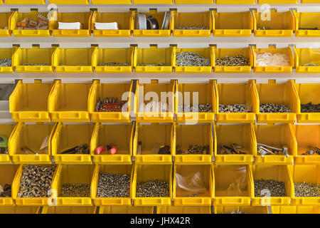 Viele gelbe Kunststoffboxen sind auf die Lichtwand in der Werkstatt hängen. In ihnen sind Schrauben, Muttern, Dübel, Bohrer, Linien, Zangen, Düsen, Stockfoto