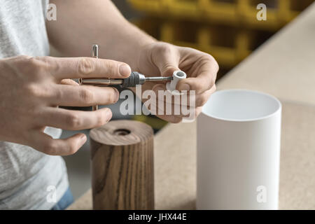 Konstruktor nutzt t-Schlüssel auf dem weißen Metall Detail in der Werkstatt. Auf dem Tisch liegen aus Holz und weißen Metall zylindrische Knüppel. Closeup. Stockfoto