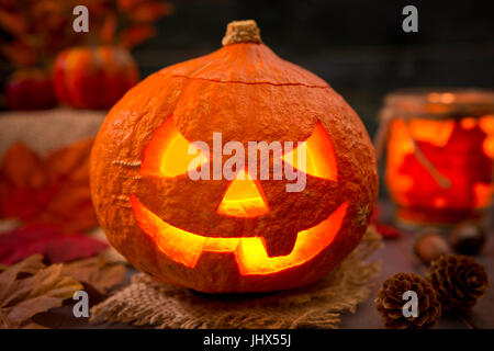 Brennen von Jack O'Lantern auf einem rustikalen Tisch mit herbstlichen Dekorationen, beleuchtet dunkel. Stockfoto