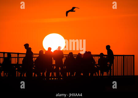 Aberystwyth, Wales, UK. 16. Juli 2017. UK-Wetter: Leute sitzen am Ende der Aberystwyths viktorianischen Seestadt Pier, Silhouette, wenn die Sonne in ein flammendes orange Himmel über Cardigan Bay auf der West-Wales untergeht Küste Photo Credit: Keith Morris/Alamy Live News Stockfoto