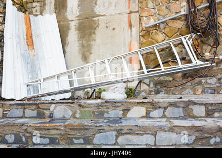Alte Holzleiter liegen auf einem Schotterweg Neigung gegen einer alten Steinmauer Stockfoto