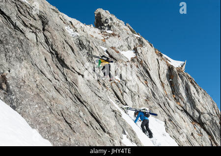 Skitour in den Bergen der Region Disentis in der Schweiz. Die Skier sind auf die Rucksäcke für den Aufstieg über eine steile Felswand montiert. Stockfoto