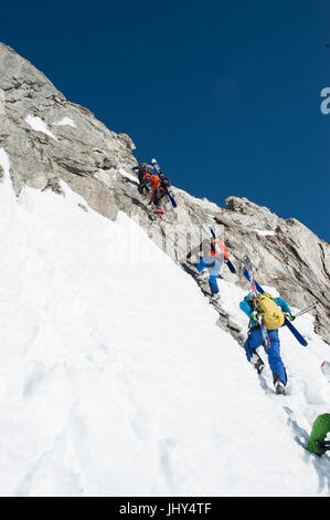 Skitour in den Bergen der Region Disentis in der Schweiz. Die Skier sind auf die Rucksäcke für den Aufstieg über eine steile Felswand montiert. Stockfoto