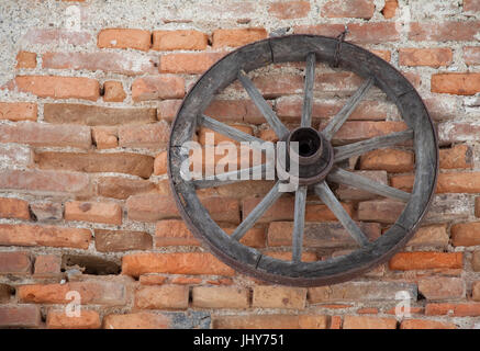Altes Wagenrad hängt von einer Mauer - alte Wagenrad hängt an einem Backstein-Flow, Altes Wagenrad Hängt ein Einer Ziegelmauer - alte Wagenrad hängen Stockfoto
