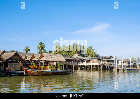 Ein Longtail-Boot und schwimmt und Stelzenläufer Häuser an einer der Grachten östlich von Krabi Stadt und Fluss, Provinz Krabi, Thailand. Stockfoto