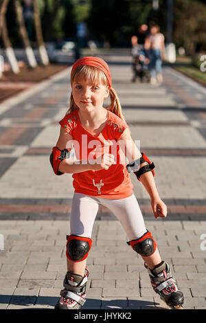 Mädchen auf Rollschuhen im Skatepark Sommer Outdoor-Reiten. Kind in einem roten Anzug für die Rollen Stockfoto