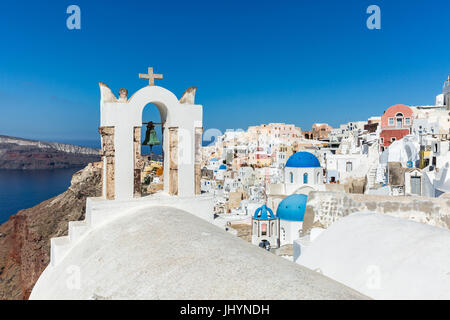 Ein Kirchendach und Bell mit dem weißen gewaschen, Steinmauern und blaue Kirche Kuppeln von Oia, Santorini, Griechenland Stockfoto