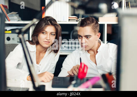 Paar junge Designer arbeiten in modernen Büros, zwei Kollegen diskutieren Spaß-Projekt über einen Laptop, kleines Team Geschäftsleute lächelnd und Blick Stockfoto