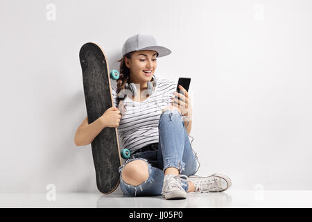 Teenager-Mädchen mit einem Skateboard mit einem Handy und auf dem Boden sitzend Stockfoto