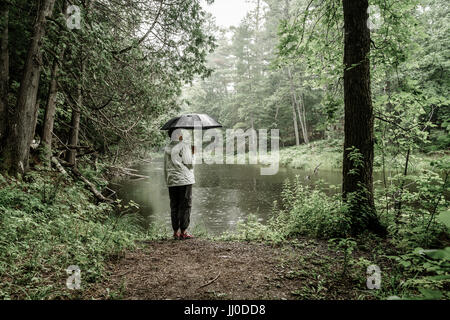 Frau mit Sonnenschirm stehend an einem Flussufer im Regen Stockfoto