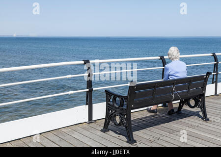 Eine reife Frau setzte sich auf eine Bank, indem sie sich mit Meerblick am Pier in Saltburn am Meer, England, Großbritannien Stockfoto