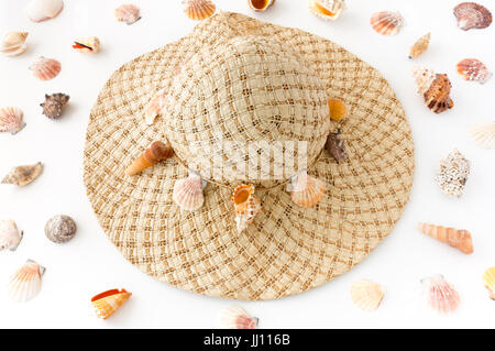 Haus dekoriert Frau Stroh Hut mit Muscheln, umgeben von einer Vielzahl von Muscheln auf weißem Hintergrund. Stockfoto