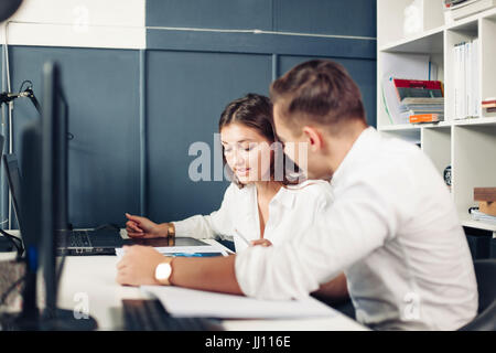 Paar junge Designer arbeiten in modernen Büros, zwei Kollegen diskutieren Spaß-Projekt über einen Laptop, kleines Team Geschäftsleute lächelnd und Blick Stockfoto