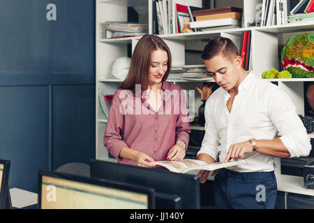 Zwei männliche Studierende Buch über marketing gemeinsam vorbereiten testen in Bibliothek sitzend und Scherz und Spaß. Kreativ blog Stockfoto