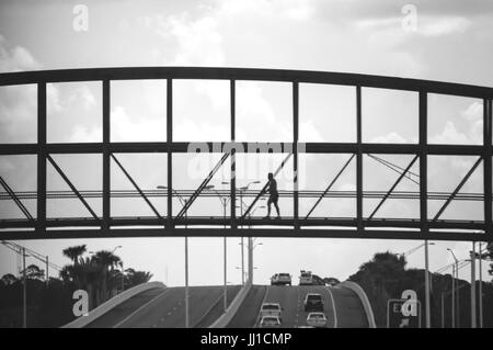 Ein Mann geht auf einer Brücke über eine Autobahn. Stockfoto