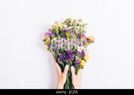 Weibliche Hände halten einen Strauß an bunten Wildblumen auf weißem Hintergrund Stockfoto