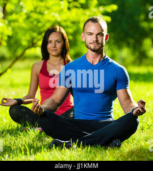 Junger Mann und Frau beim Yoga im sonnigen Sommerpark Stockfoto