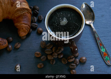 frisch gemahlener Kaffee mit Croissant auf schwarzem Schiefer. niedrigen Winkel Closeup zurückhaltend erschossen Stockfoto