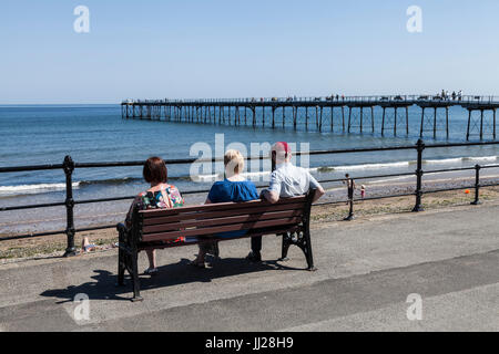 Drei Leute saßen auf einer Bank, Blick auf das Meer bei Saltburn am Meer, England, UK Stockfoto