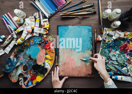 Maler am Arbeitsplatz Draufsicht Foto. Künstler-Pinsel, bunte Farben und Stifte sortiert auf dem Schreibtisch. Stockfoto