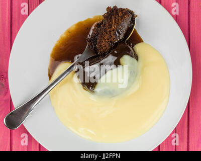 Sticky Toffee Pudding Dessert serviert mit heißen Pudding vor einem rosa Hintergrund aus Holz Stockfoto