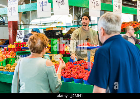 Montreal, Kanada - 27. Mai 2017: Mann, Verkauf von Produkten durch Obststand mit Frau kauft Erdbeeren auf Jean-Talon Bauernmarkt mit displays Stockfoto