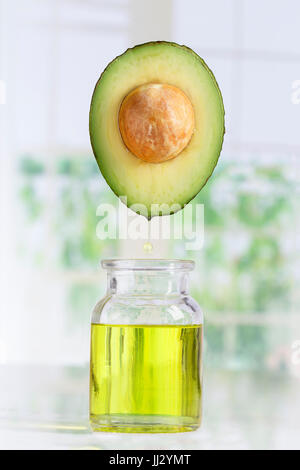 Frische Avocado und Öl fallen in einer Flasche auf weiß Stockfoto