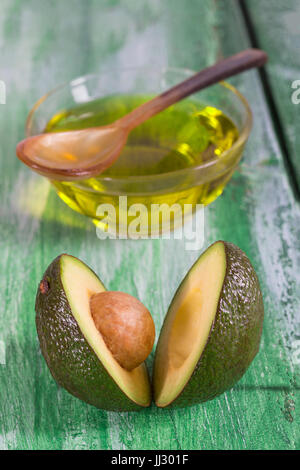 Frische ganze und geschnittene Avocado und eine Tasse Öl Ongreen craked hölzernen Tisch - kochen, medizinisches Konzept Stockfoto