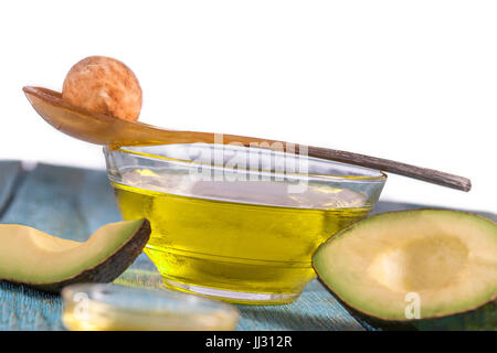 Frische ganze und geschnittene Avocado und eine Tasse Öl Ongreen craked hölzernen Tisch - Küche, Wellness, Bodycare-Konzept Stockfoto