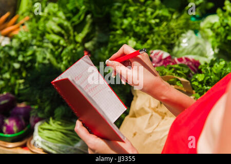 Eine Frau kreuzt, Käufe von Einkaufsliste. Mädchen mit einem Notebook in Händen. Stockfoto