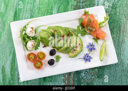 Toast mit Avocado und geräuchertem Lachs auf den weißen Teller auf alten grünen craked Holzbrett Stockfoto