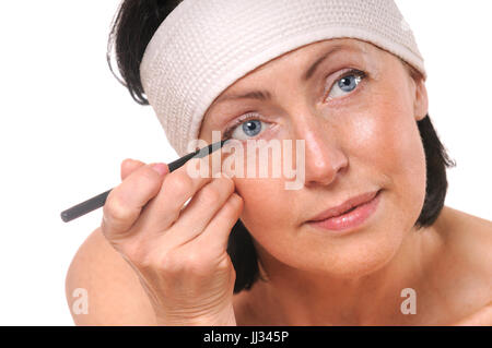 Porträt von fokussierten Blick in die Kamera während putting Eyeliner Frau hautnah. Isoliert auf weiss. Alte Haut Pflegekonzept Stockfoto