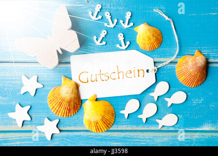 Flach legen Ansicht des Labels mit deutschem Text Gutschein bedeutet Gutschein. Sonnigen Gruß Card Schmetterling, Muscheln und Fische auf blauem Hintergrund aus Holz Stockfoto