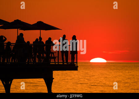 Aberystwyth Wales UK, Montag, 17. Juli 2017 UK Wetter: Menschen auf Aberystwyth Pier sind in den lebendigen goldenen Sonnenuntergang über den ruhigen Gewässern der Cardigan Bay, Silhouette, wie die Mini-Hitzewelle beginnt, über das UK Foto Kredit bauen: Keith Morris/Alamy Live News Stockfoto