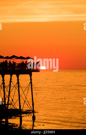 Aberystwyth Wales UK, Montag, 17. Juli 2017 UK Wetter: Menschen auf Aberystwyth Pier sind in den lebendigen goldenen Sonnenuntergang über den ruhigen Gewässern der Cardigan Bay, Silhouette, wie die Mini-Hitzewelle beginnt, über das UK Foto Kredit bauen: Keith Morris/Alamy Live News Stockfoto