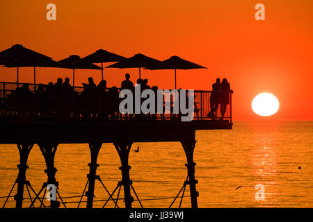 Aberystwyth Wales UK, Montag, 17. Juli 2017 UK Wetter: Menschen auf Aberystwyth Pier sind in den lebendigen goldenen Sonnenuntergang über den ruhigen Gewässern der Cardigan Bay, Silhouette, wie die Mini-Hitzewelle beginnt, über das UK Foto Kredit bauen: Keith Morris/Alamy Live News Stockfoto