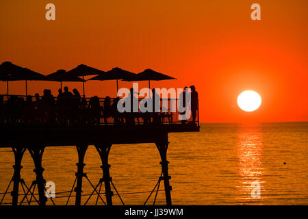 Aberystwyth Wales UK, Montag, 17. Juli 2017 UK Wetter: Menschen auf Aberystwyth Pier sind in den lebendigen goldenen Sonnenuntergang über den ruhigen Gewässern der Cardigan Bay, Silhouette, wie die Mini-Hitzewelle beginnt, über das UK Foto Kredit bauen: Keith Morris/Alamy Live News Stockfoto