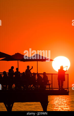 Aberystwyth Wales UK, Montag, 17. Juli 2017 UK Wetter: Menschen auf Aberystwyth Pier sind in den lebendigen goldenen Sonnenuntergang über den ruhigen Gewässern der Cardigan Bay, Silhouette, wie die Mini-Hitzewelle beginnt, über das UK Foto Kredit bauen: Keith Morris/Alamy Live News Stockfoto