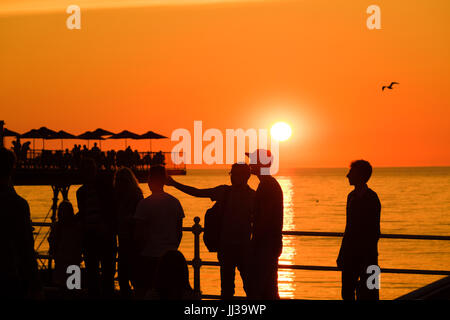 Aberystwyth Wales UK, Montag, 17. Juli 2017 UK Wetter: Menschen auf Aberystwyth Pier sind in den lebendigen goldenen Sonnenuntergang über den ruhigen Gewässern der Cardigan Bay, Silhouette, wie die Mini-Hitzewelle beginnt, über das UK Foto Kredit bauen: Keith Morris/Alamy Live News Stockfoto