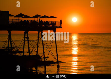 Aberystwyth Wales UK, Montag, 17. Juli 2017 UK Wetter: Menschen auf Aberystwyth Pier sind in den lebendigen goldenen Sonnenuntergang über den ruhigen Gewässern der Cardigan Bay, Silhouette, wie die Mini-Hitzewelle beginnt, über das UK Foto Kredit bauen: Keith Morris/Alamy Live News Stockfoto