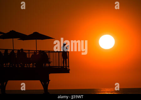 Aberystwyth Wales UK, Montag, 17. Juli 2017 UK Wetter: Menschen auf Aberystwyth Pier sind in den lebendigen goldenen Sonnenuntergang über den ruhigen Gewässern der Cardigan Bay, Silhouette, wie die Mini-Hitzewelle beginnt, über das UK Foto Kredit bauen: Keith Morris/Alamy Live News Stockfoto