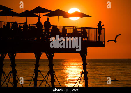 Aberystwyth Wales UK, Montag, 17. Juli 2017 UK Wetter: Menschen auf Aberystwyth Pier sind in den lebendigen goldenen Sonnenuntergang über den ruhigen Gewässern der Cardigan Bay, Silhouette, wie die Mini-Hitzewelle beginnt, über das UK Foto Kredit bauen: Keith Morris/Alamy Live News Stockfoto