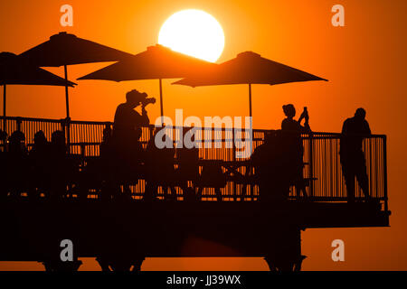 Aberystwyth Wales UK, Montag, 17. Juli 2017 UK Wetter: Menschen auf Aberystwyth Pier sind in den lebendigen goldenen Sonnenuntergang über den ruhigen Gewässern der Cardigan Bay, Silhouette, wie die Mini-Hitzewelle beginnt, über das UK Foto Kredit bauen: Keith Morris/Alamy Live News Stockfoto