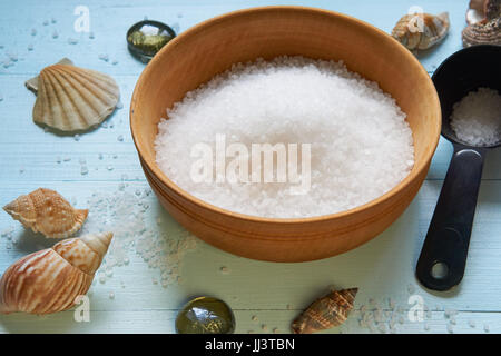 große Holzschale mit mineralischen Meersalz mit schwarzen Kugel gefüllt mit Salz beiseite auf Licht blau lackierten hölzernen Schreibtisch. niedrigen Winkel-Detailansicht Stockfoto