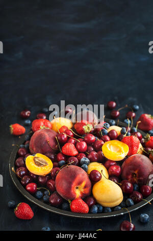 Frische reife Sommerbeeren und Früchte (Pfirsiche, Aprikosen, Kirschen und Erdbeeren) auf Tablett Stockfoto